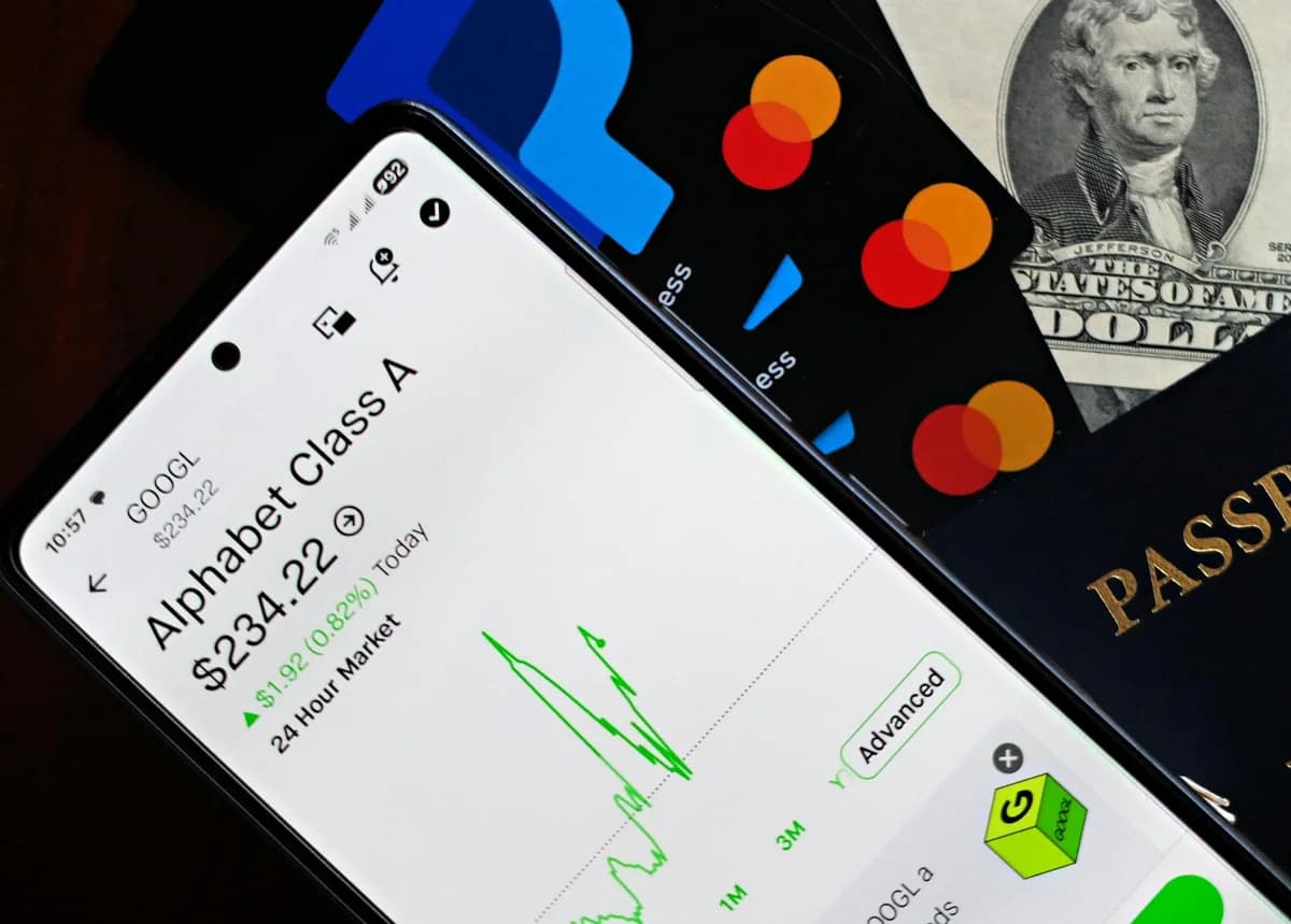 A smartphone displaying Alphabet stock price alongside credit cards, cash, and passport.
