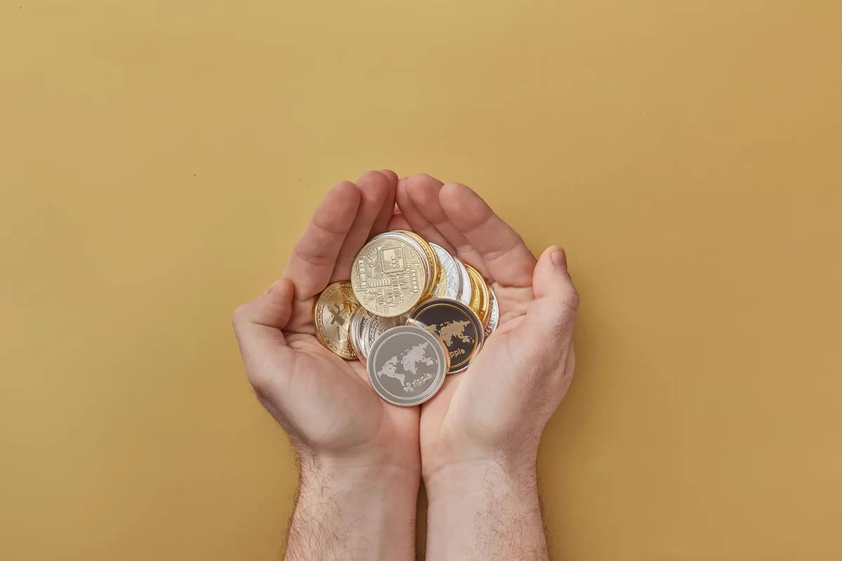 Close-up of hands scooping assorted cryptocurrency coins into a jar on a wooden surface.