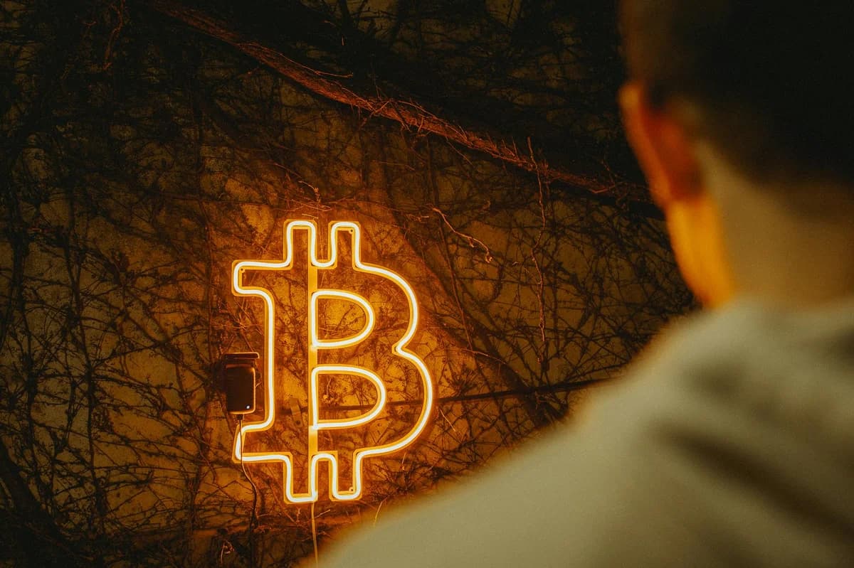 Image of a US 100 dollar bill and a Bitcoin coin on a black background, symbolizing traditional and digital currency.