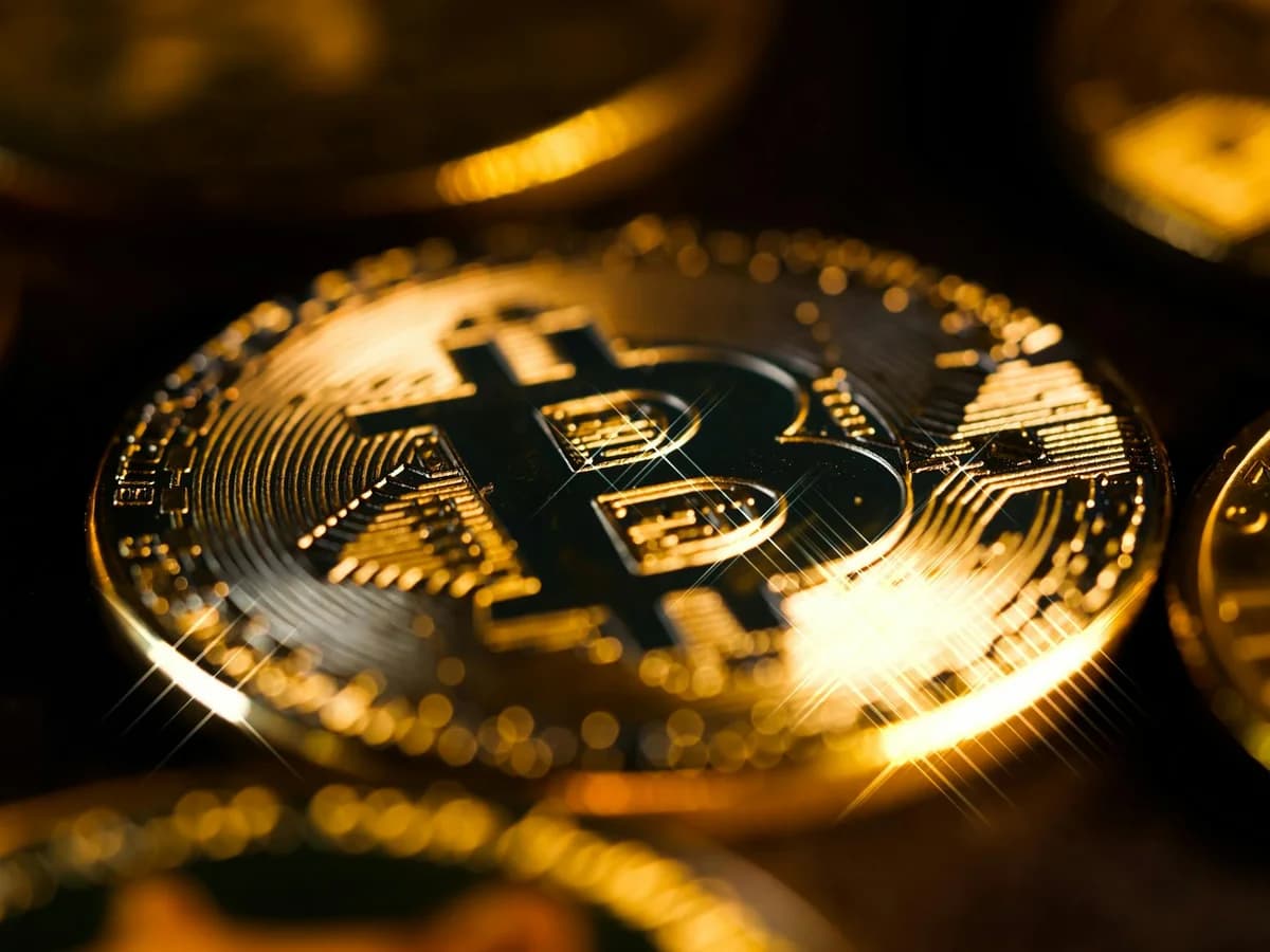 A stack of gold Bitcoin coins placed on a shimmering gold glitter background.
