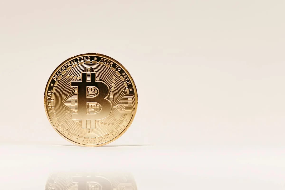 Close-up of a golden Bitcoin coin standing upright on a neutral background, showcasing cryptocurrency symbolism.