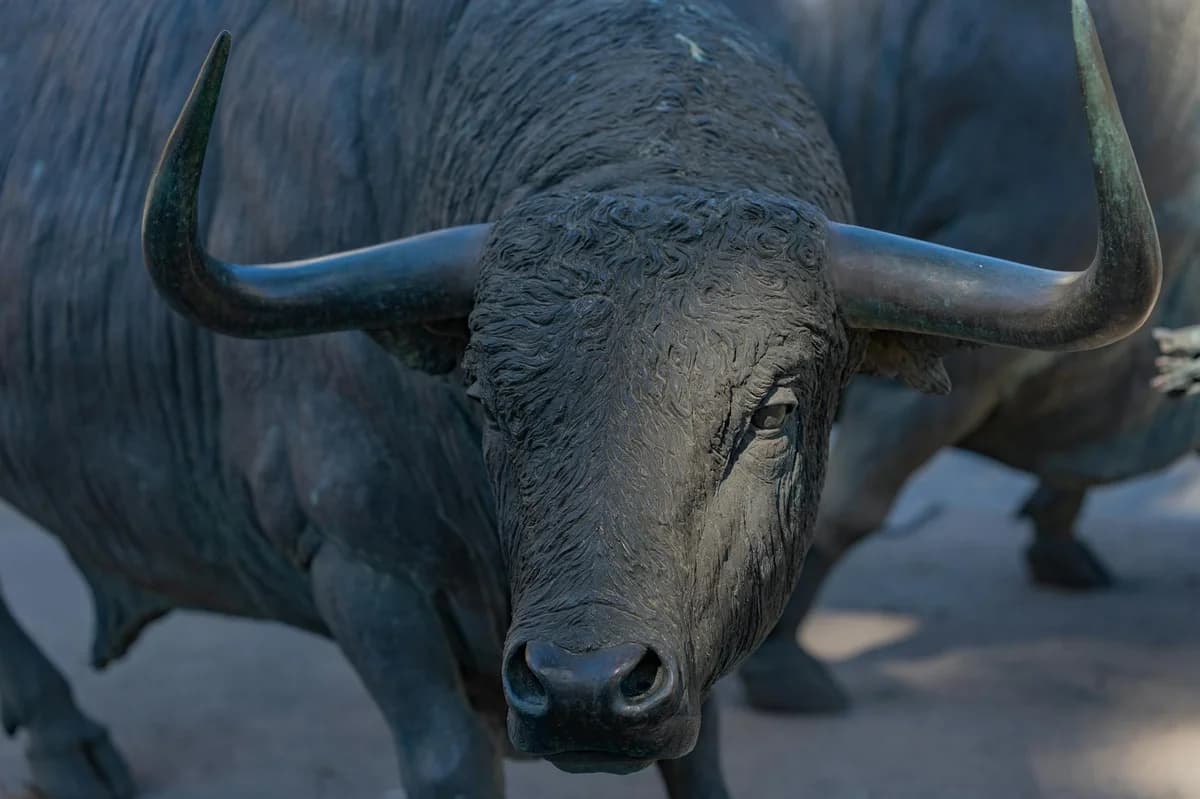 Close-up of a bronze bull statue outdoors, showcasing its powerful horns and detailed craftsmanship.