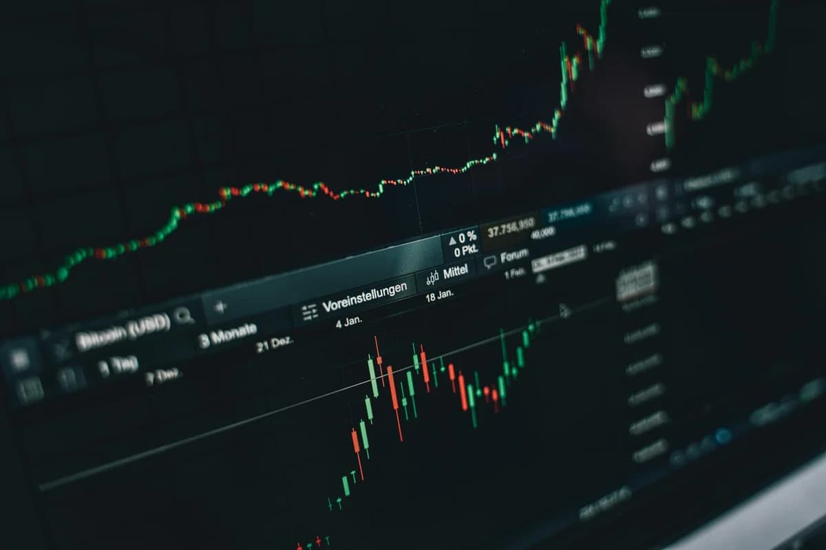 Smartphone displaying trading app with Bitcoin coins on a dark surface.