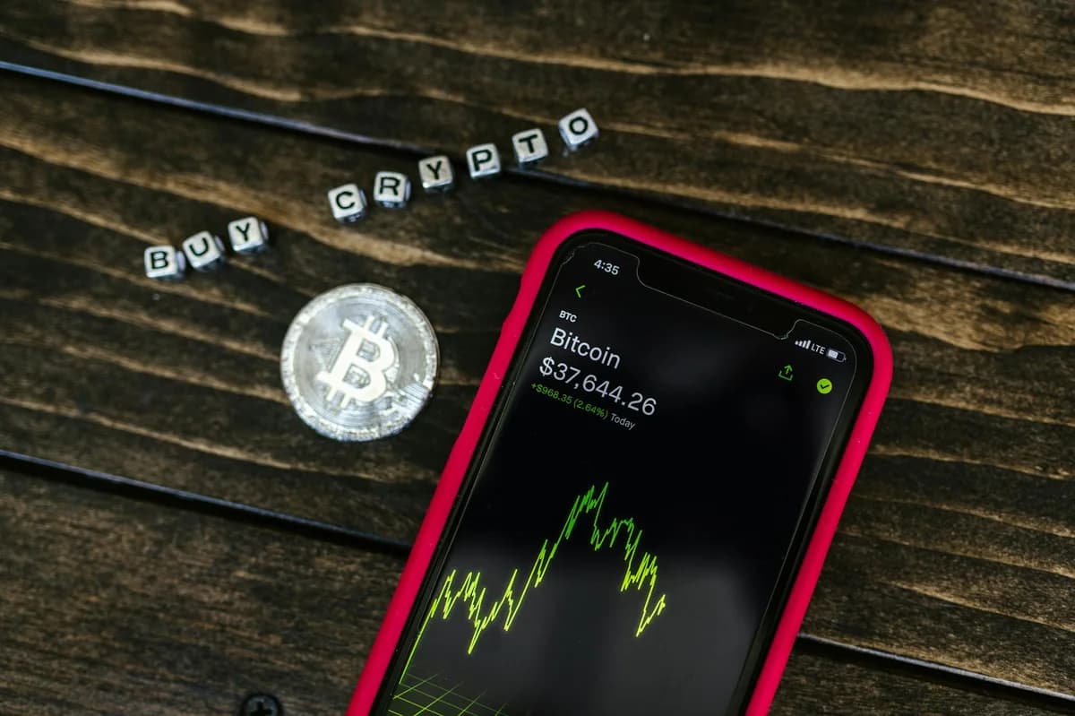 Close-up of a smartphone app showing Bitcoin trading details with crypto coins on a black surface.