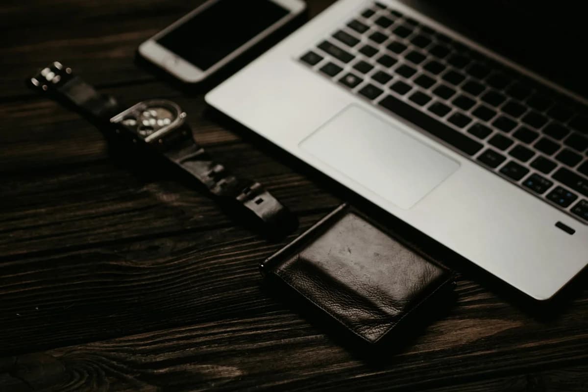 A hand holding a smartphone displaying a blockchain app, with a laptop on a desk in the background.