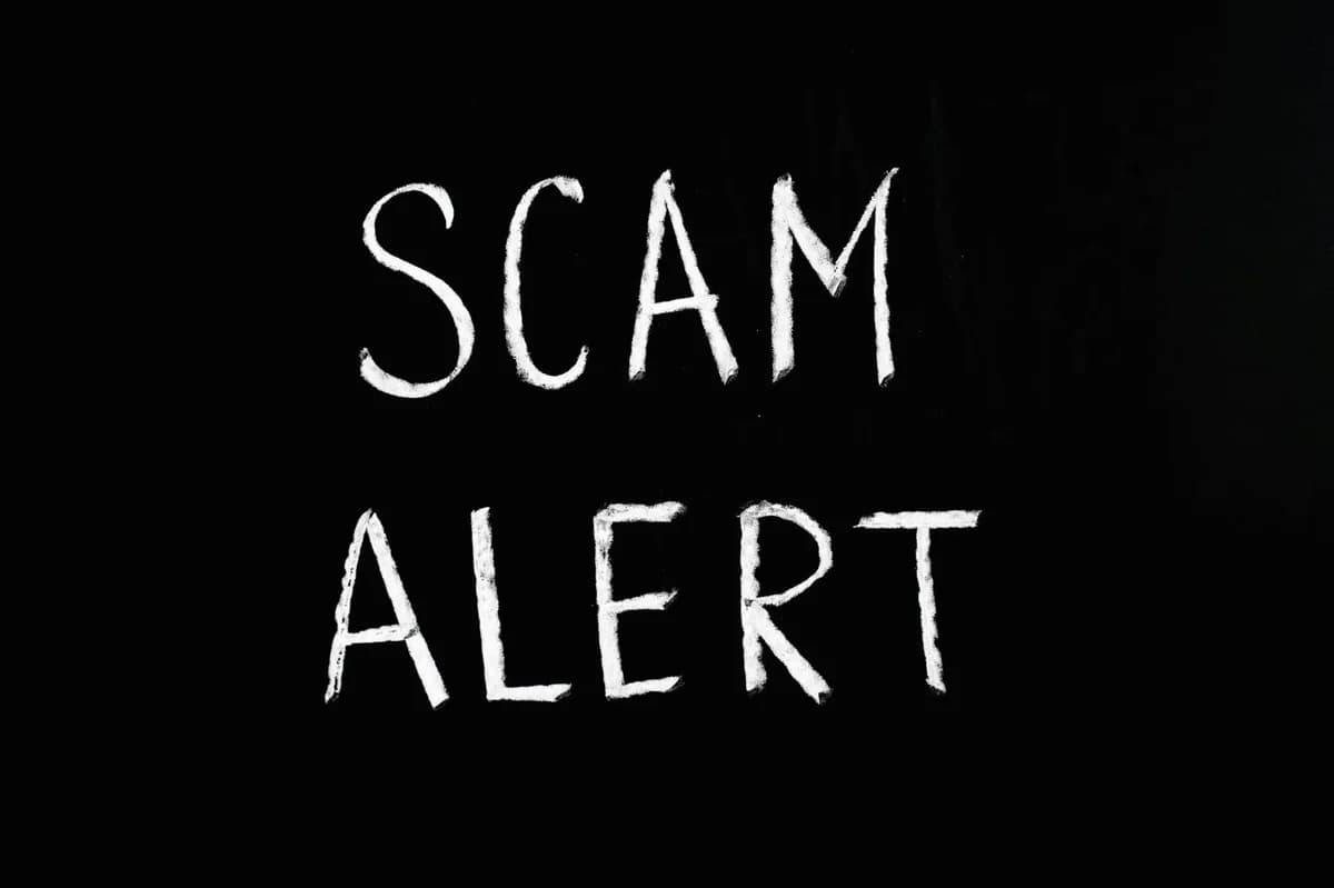 Business person holding a scam alert sign over a laptop, warning against online fraud.