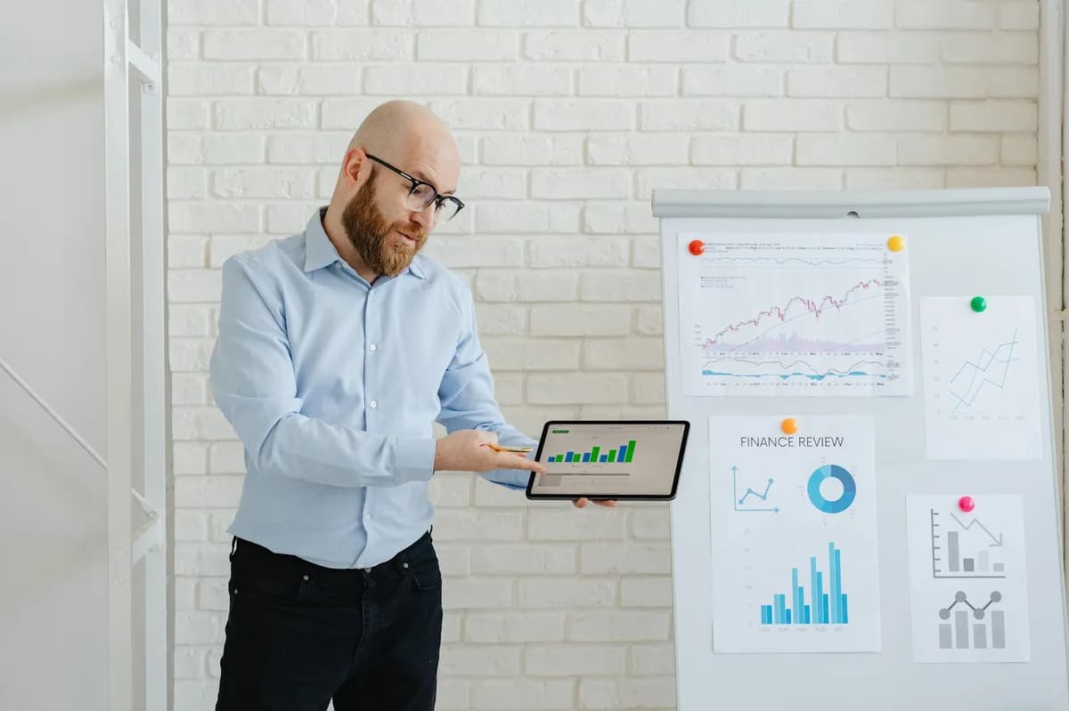 A woman points at a stock market chart on a whiteboard, explaining financial trends.