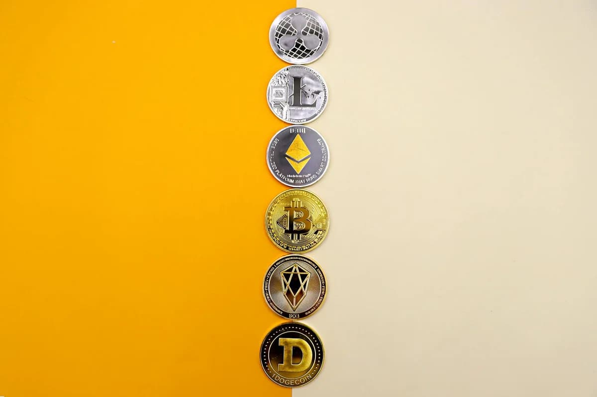 A row of cryptocurrency coins including Bitcoin, Ethereum, and Dogecoin on a vibrant yellow surface.