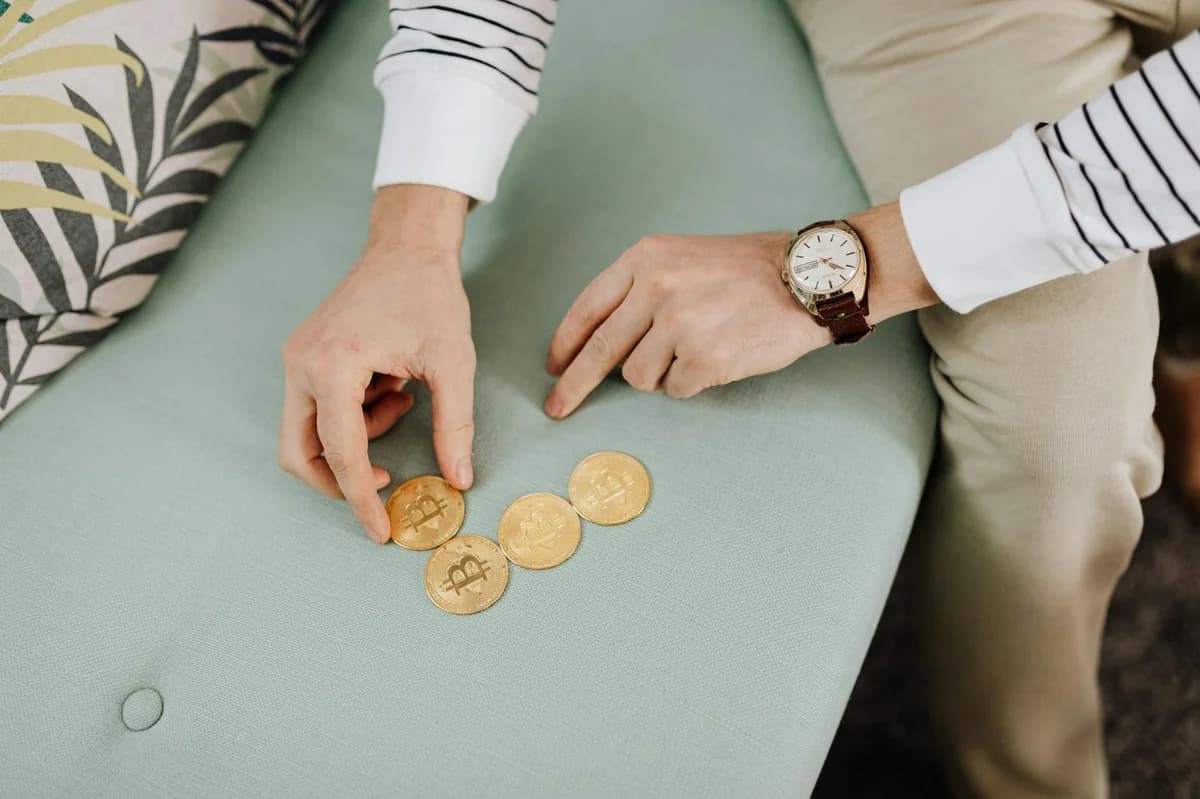 Close-up of hands holding bitcoin coins on a green sofa, emphasizing digital currency trends.