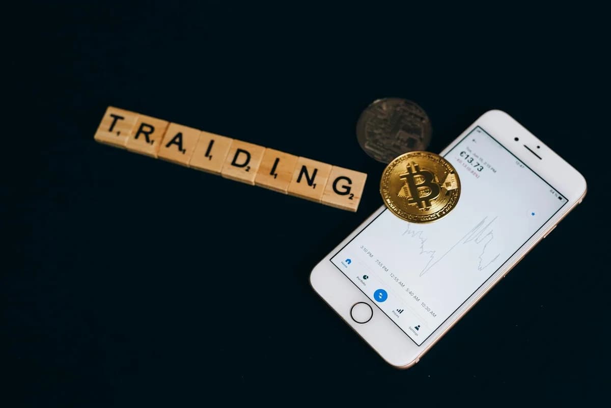 Close-up of a smartphone app showing Bitcoin trading details with crypto coins on a black surface.