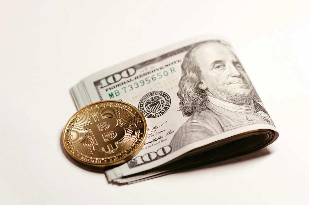 Bitcoin coin standing in front of a 100 dollar bill, symbolizing cryptocurrency and traditional currency themes.