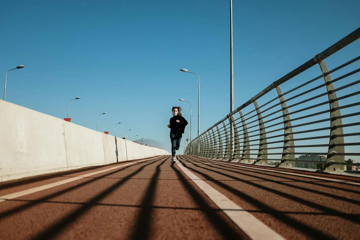 A woman runs on an empty urban bridge with modern architecture under a clear blue sky.