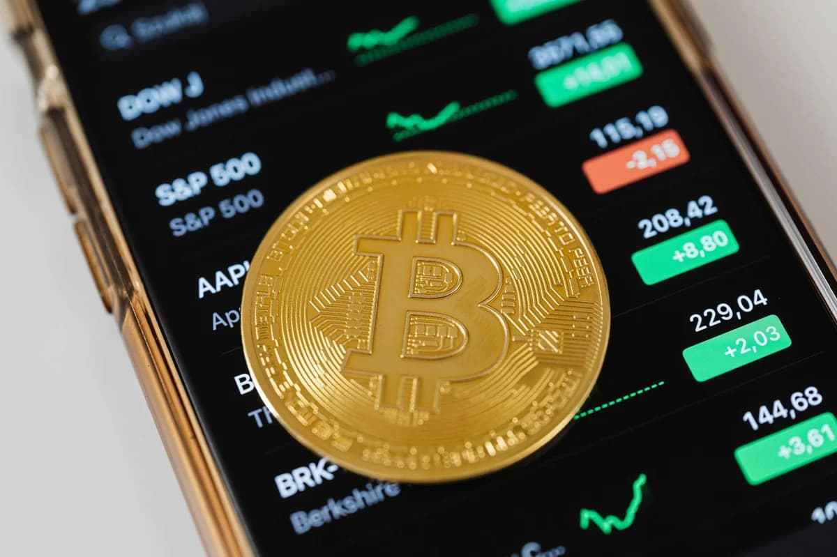 Golden mug with 'Bitcoin Millionaire' text in front of stock market charts on laptop screen.