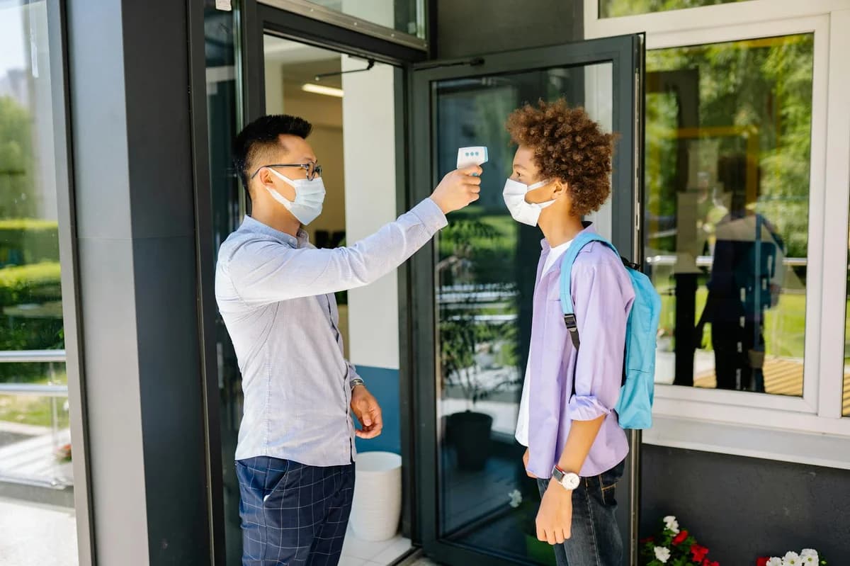 Teacher checks student's temperature with an infrared thermometer outside school.
