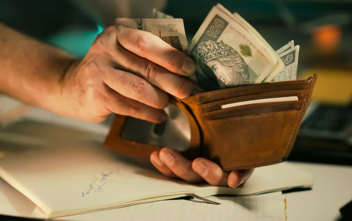 A close-up of hands holding a wallet filled with Polish banknotes on a desk.