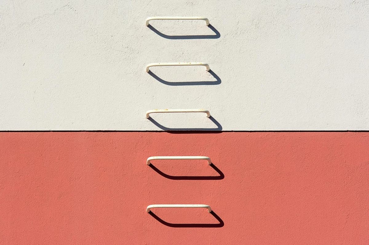 A minimalist view of a metal ladder casting shadows on a divided white and red wall.