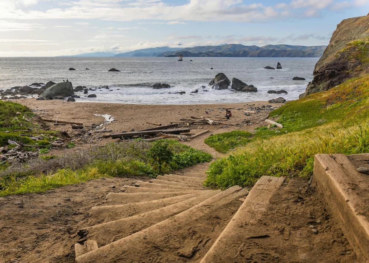 Tranquil beach scene with steps leading to a rocky shore under a calm sky.