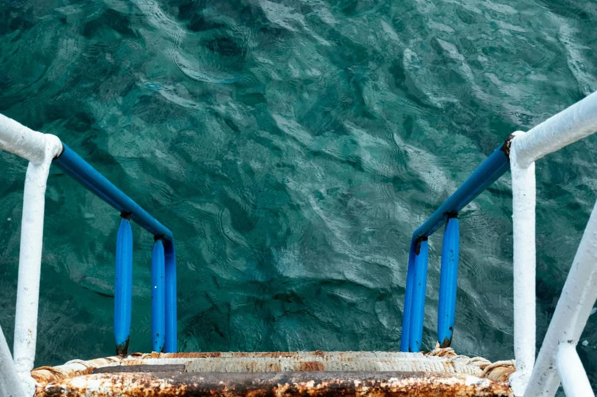 View of rusty metal stairs descending into clear turquoise seawater, evoking a sense of adventure.