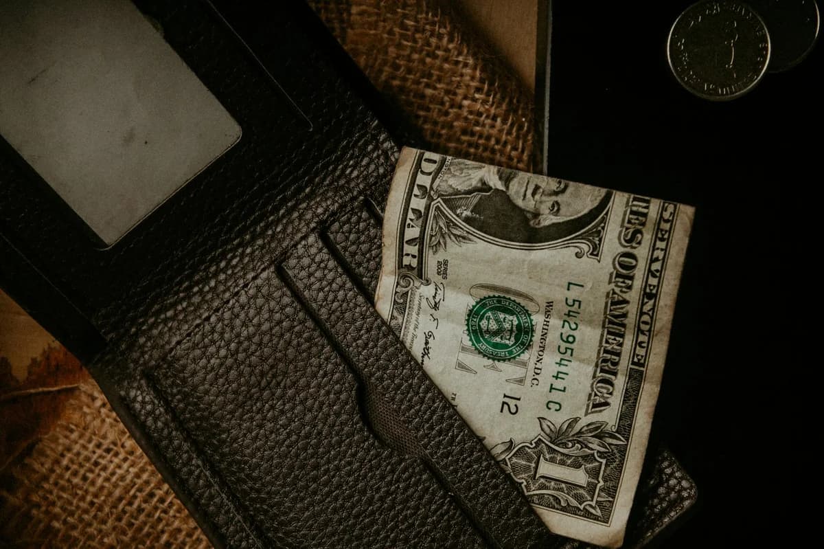 A close-up view of a leather wallet with a one dollar bill and coins, highlighting personal finance concepts.