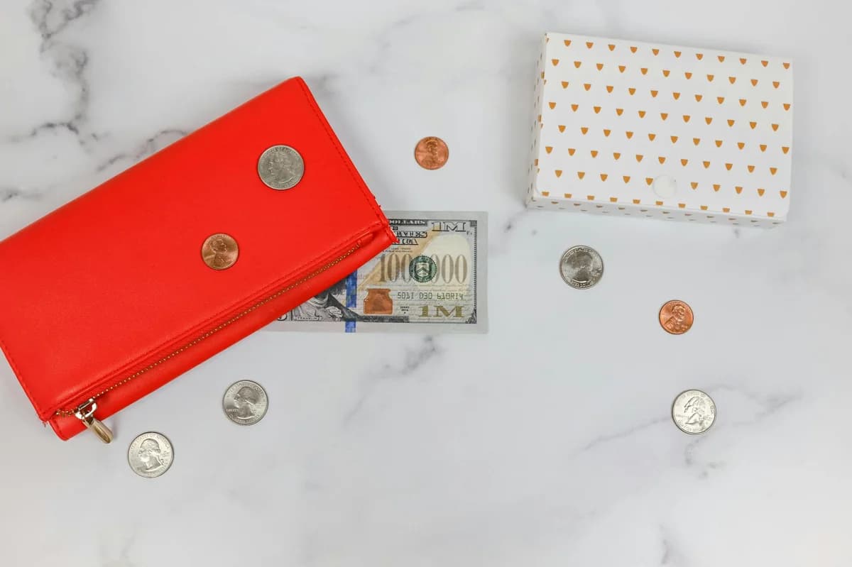 Hands holding a leather wallet with cash and a credit card on a wooden surface.
