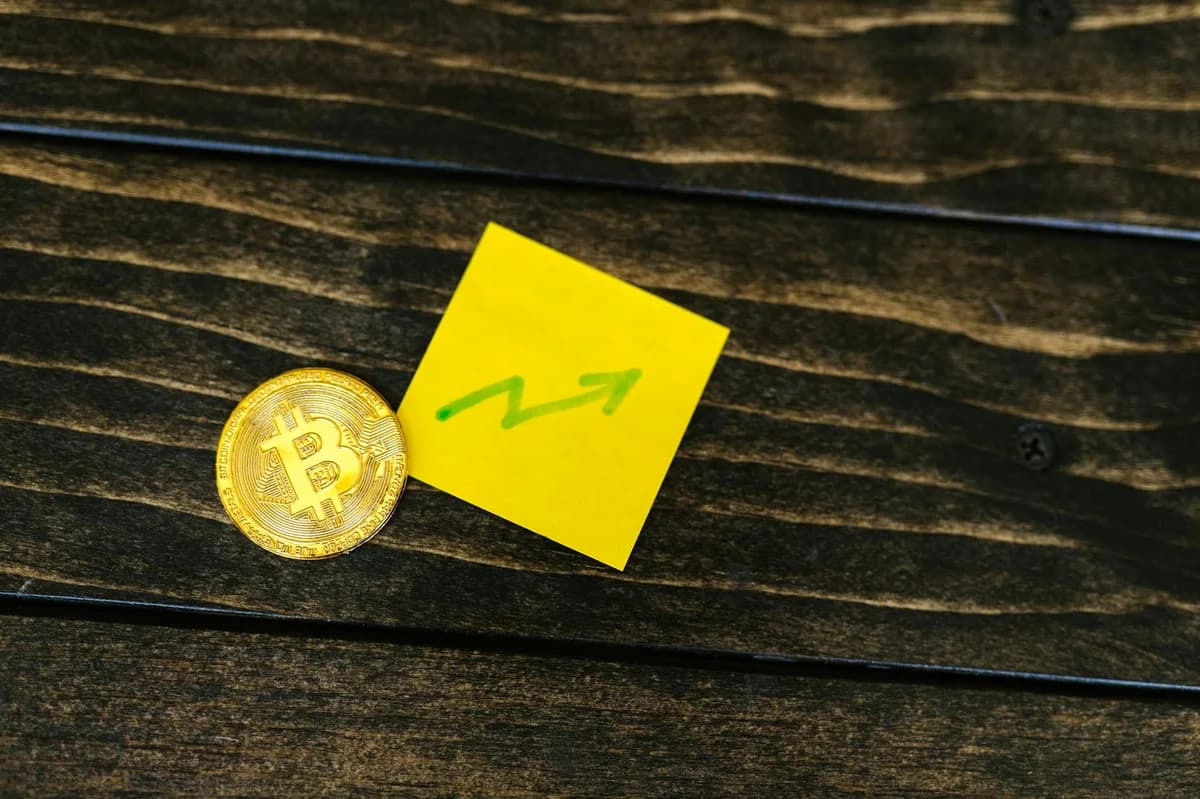 Smartphone displaying financial chart with Bitcoin coins on pink background.