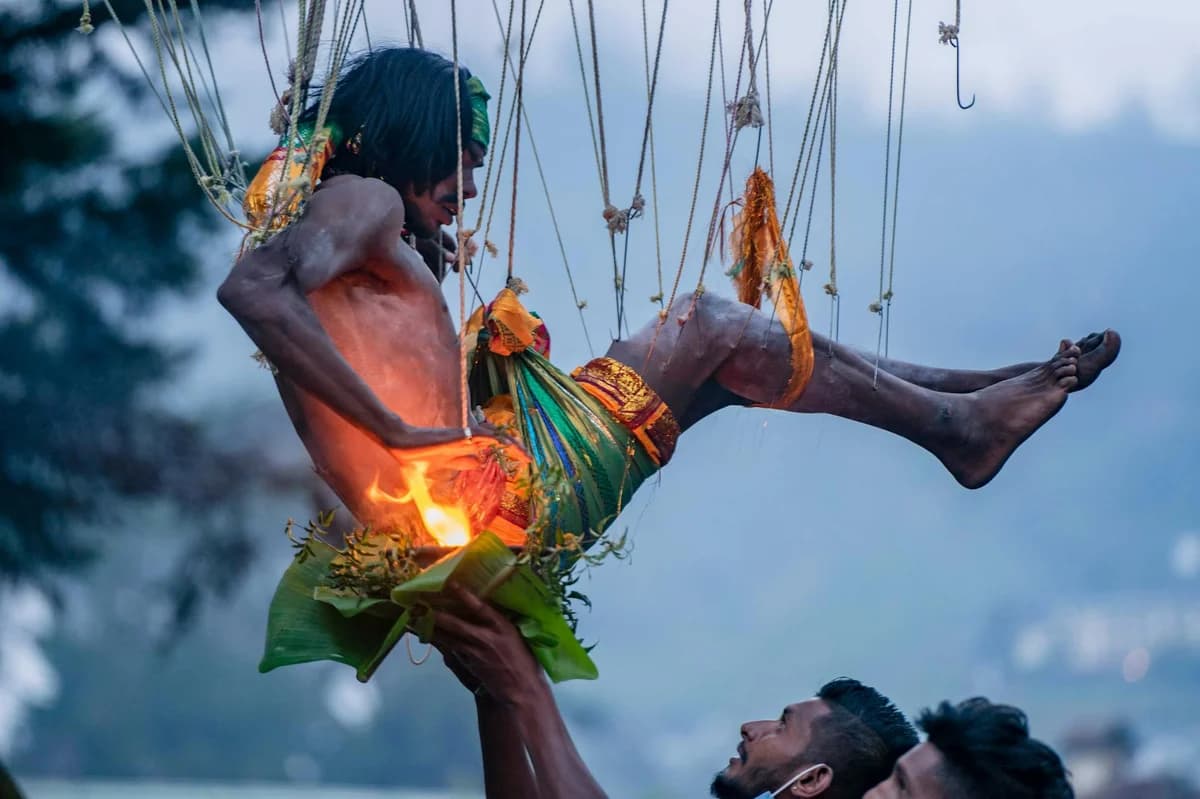 A man performs a suspension ritual in traditional clothing during a festival.