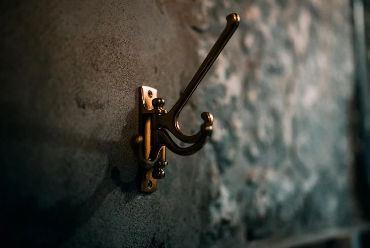 Close-up of a brass coat hook mounted on a textured wall, creating a rustic ambiance indoors.