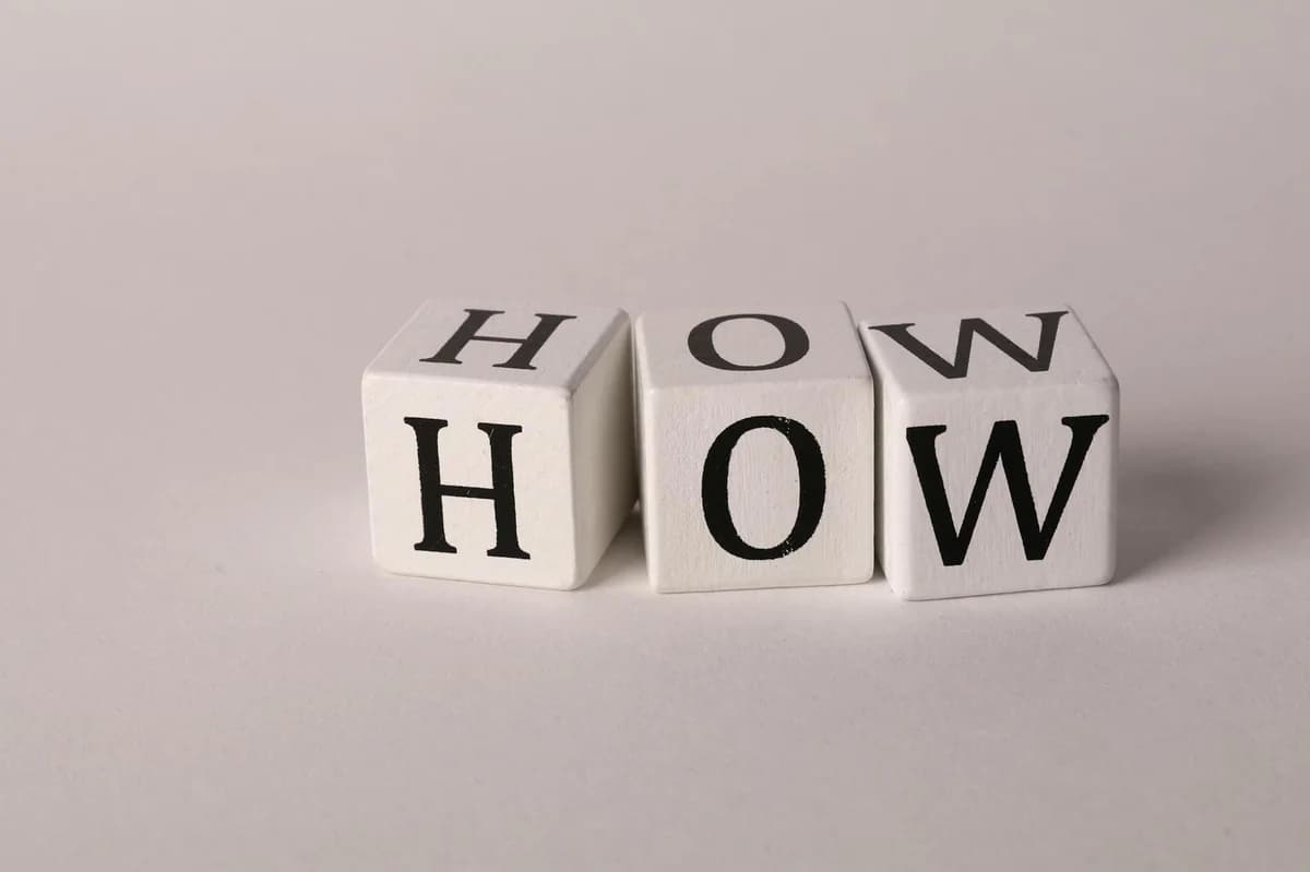 Close-up of white wooden cubes with the letters 'H', 'O', and 'W' arranged on a neutral background.
