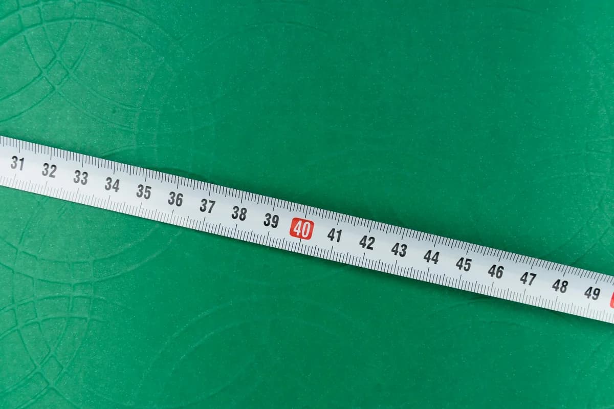 A measuring tape lying diagonally on a green textured surface.