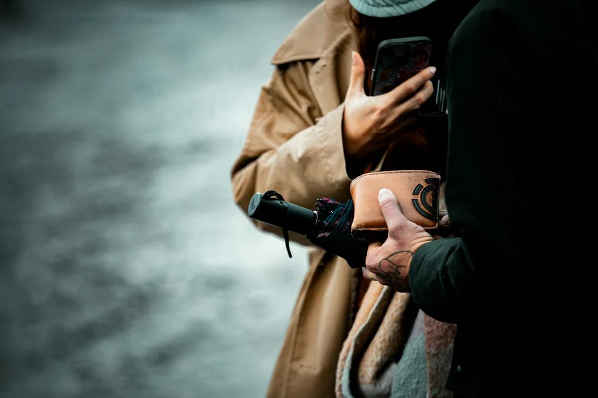 Close-up of urban interaction with a folded umbrella, wallet, and hand tattoo in fall attire.