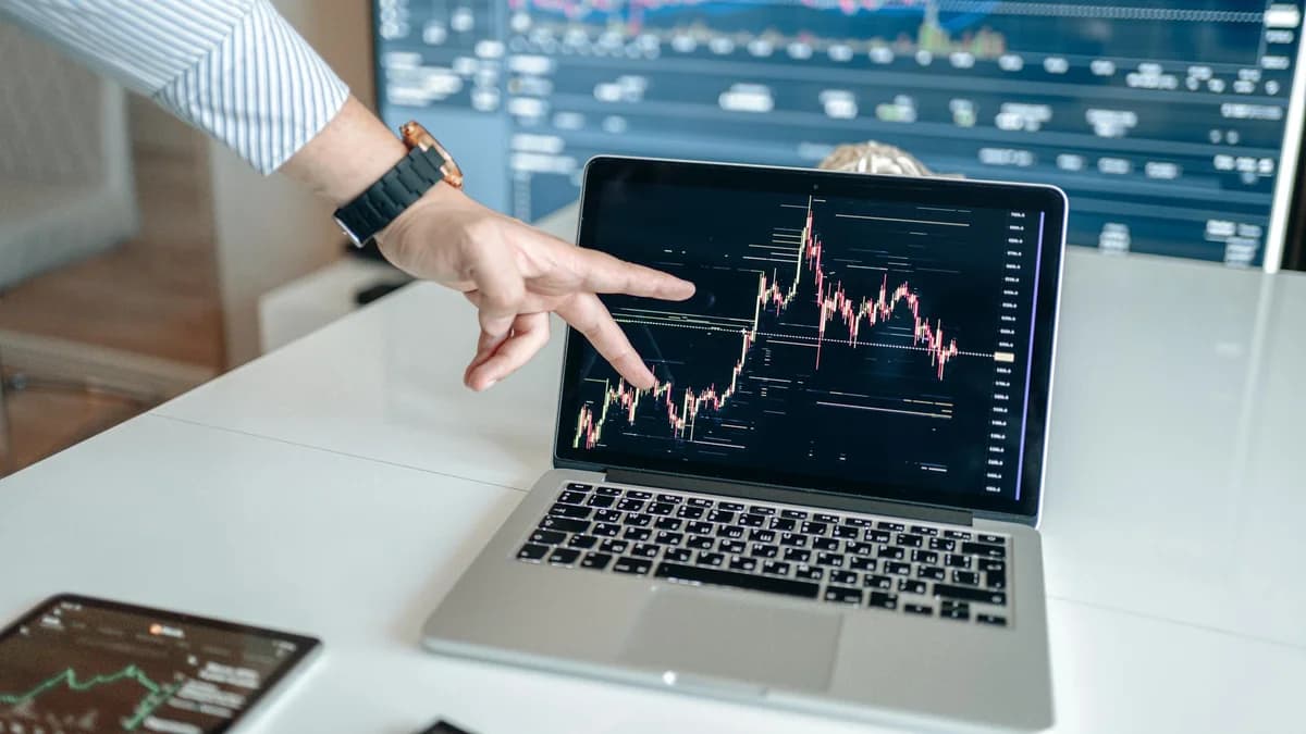 Hands typing on a laptop displaying financial trading charts, indicating active online trading work.
