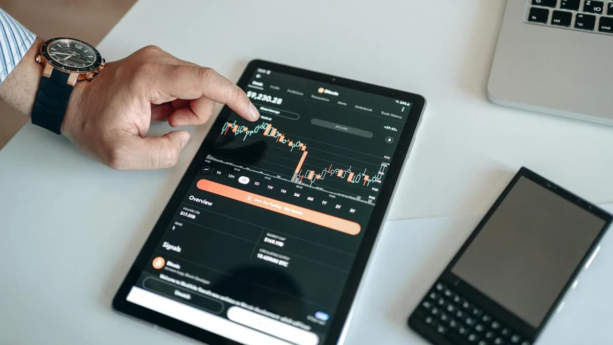 Flat lay of Bitcoin coins, smartphone with graph, and glasses on gray surface.