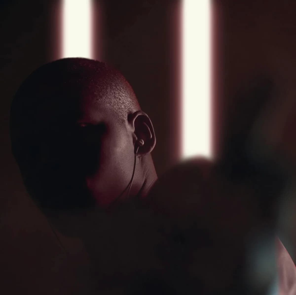 Dark and moody portrait of a person in earphones, highlighted by vertical backlights.