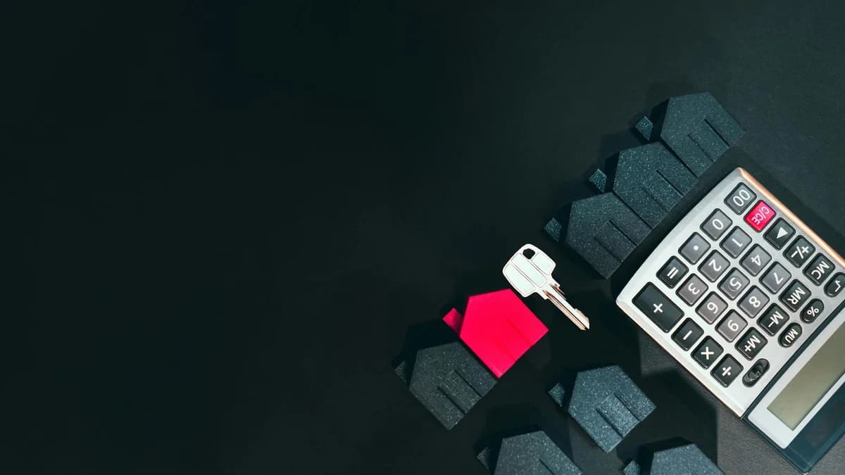 Real estate concept image featuring a calculator, houses, and a key on a black background.
