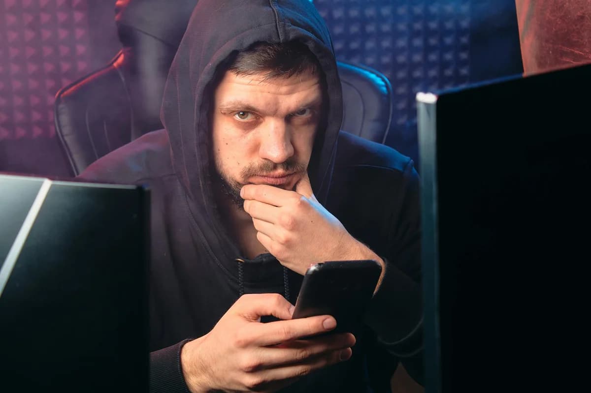An anonymous hacker wearing a mask working on a computer in a dark room.