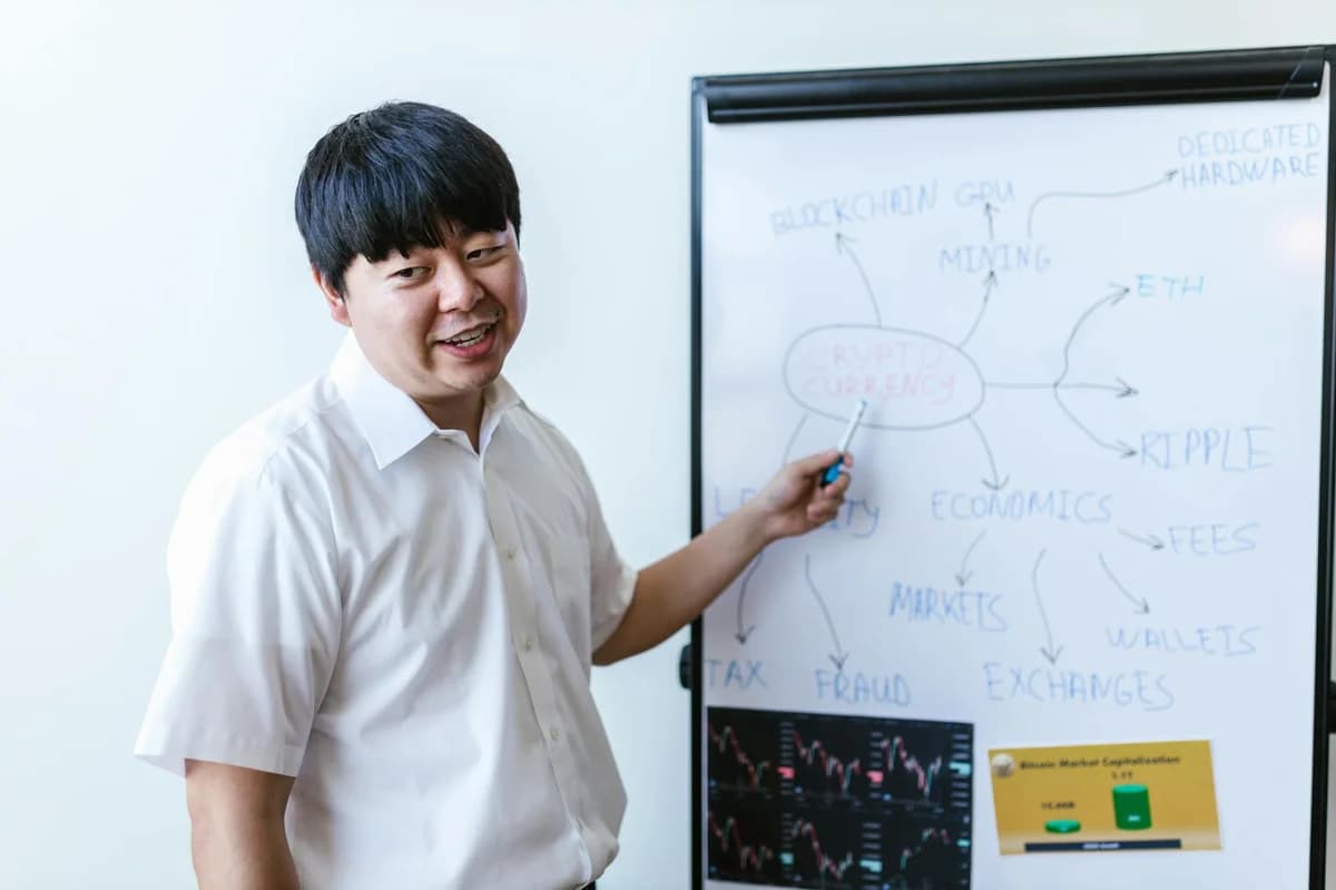 Man explaining cryptocurrency concepts on a whiteboard in a modern office setting.