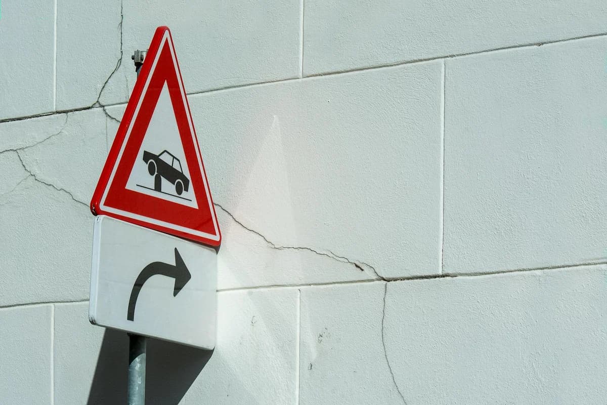 Traffic warning sign on a cracked white wall, indicating a turn ahead.