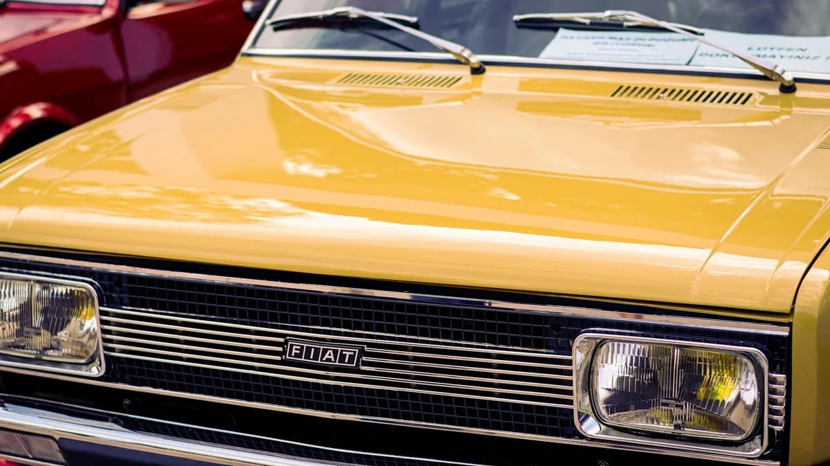 Closeup of a vintage yellow Fiat car's front grill and headlights.