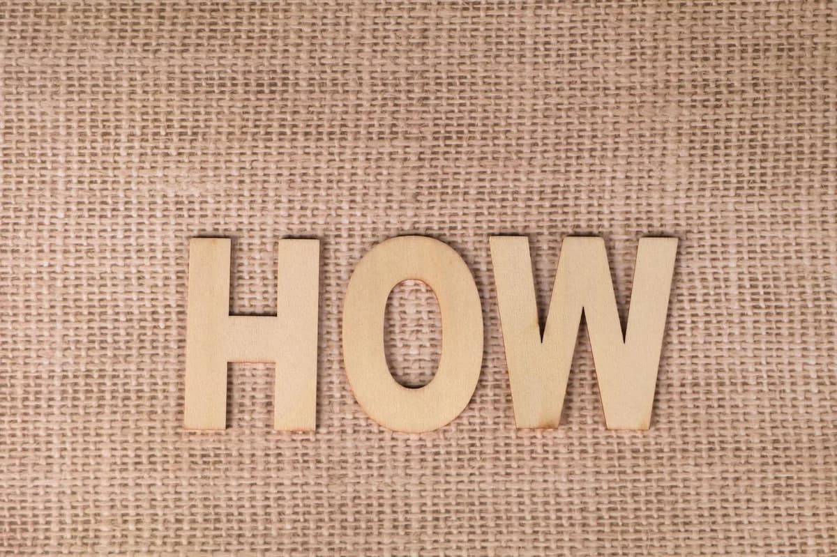 Word 'HOW' formed with wooden letters on textured burlap surface.