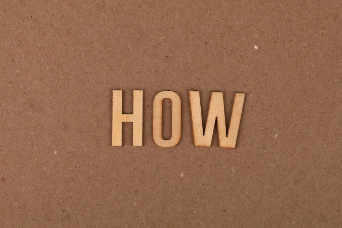 Wooden letters spelling 'HOW' on brown textured cardboard background.