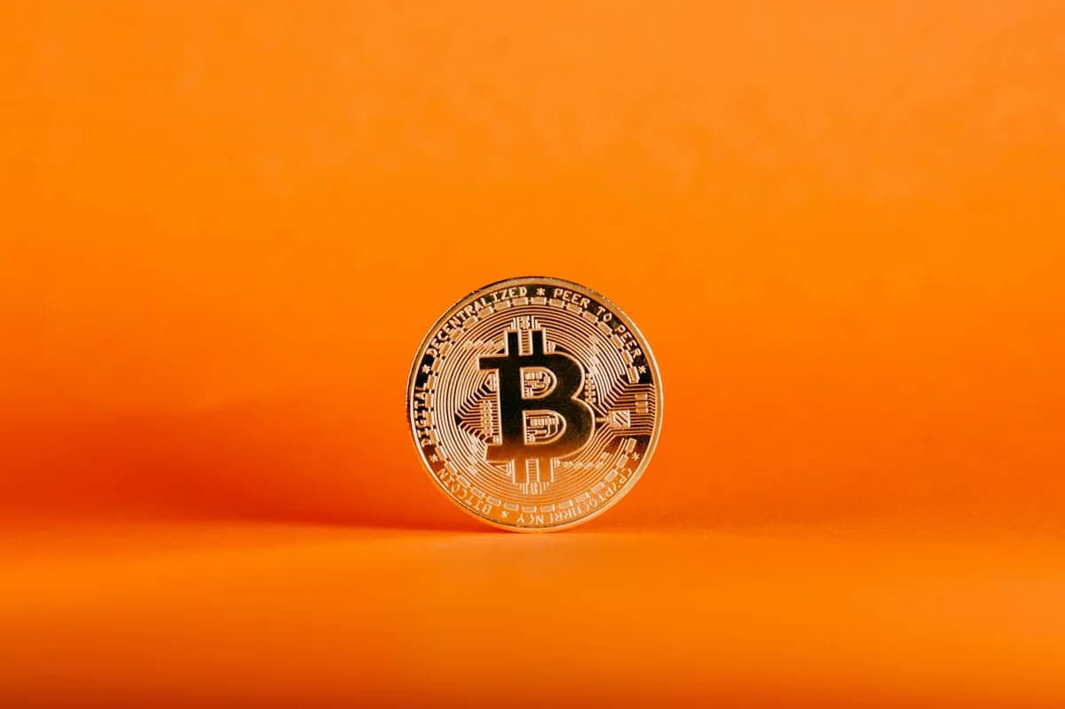 Close-up of a Bitcoin coin on an orange background, symbolizing digital cryptocurrency.