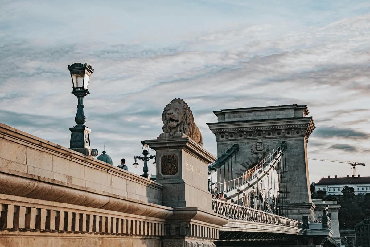 Iconic Széchenyi Chain Bridge in Budapest with tourists and lion sculptures on a clear day.
