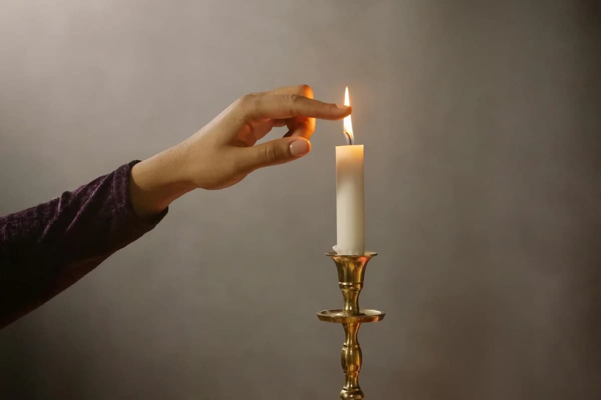 A hand gently lights a single candle flame on a brass holder, creating a serene atmosphere.