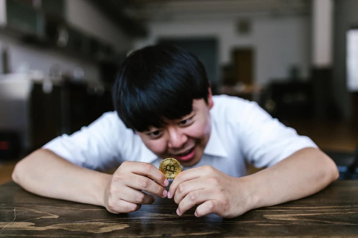 A young man excitedly examining a Bitcoin coin in an indoor setting.