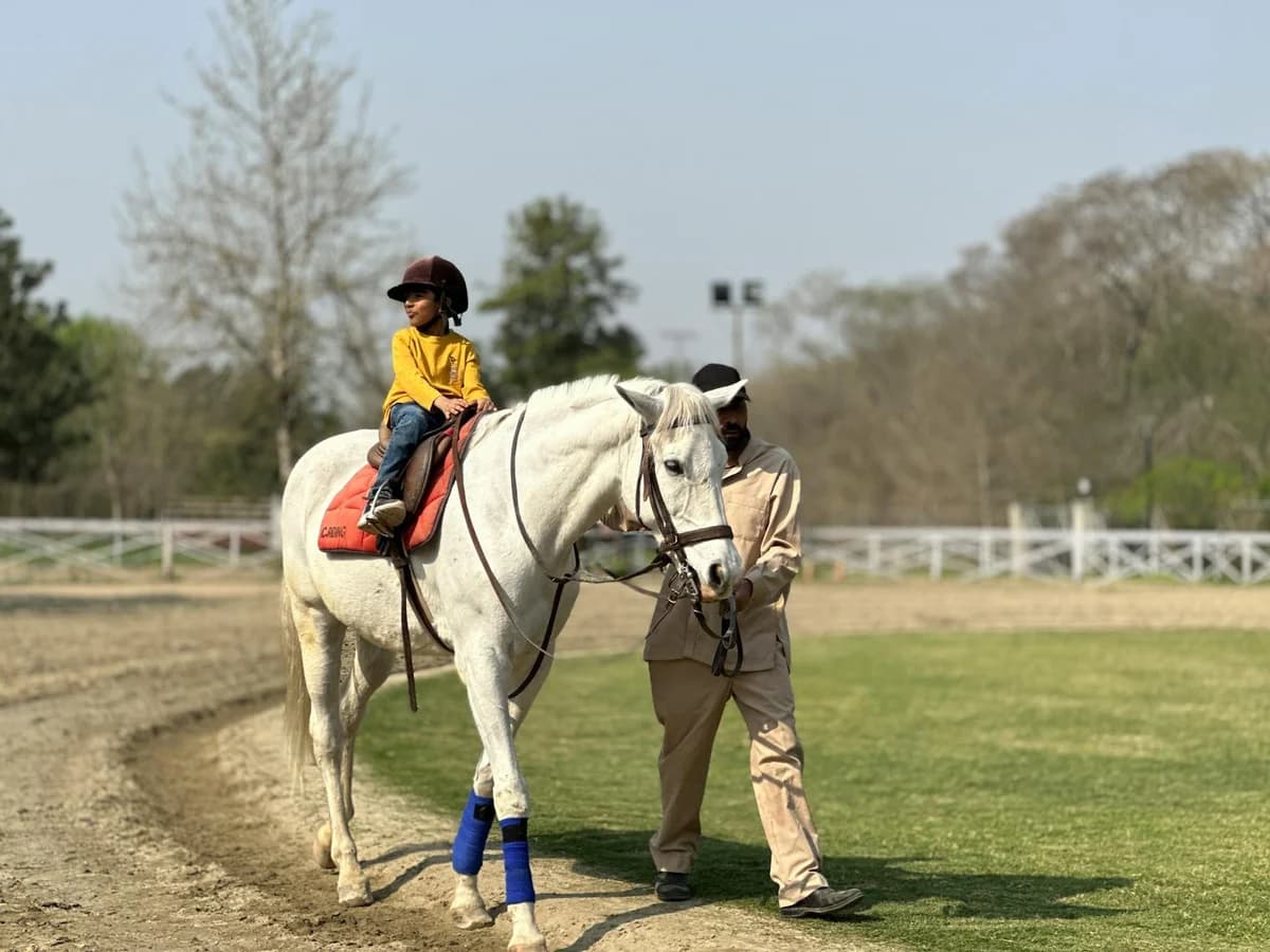 A young child enjoys a horseback ride with guidance in a serene Islamabad park setting.