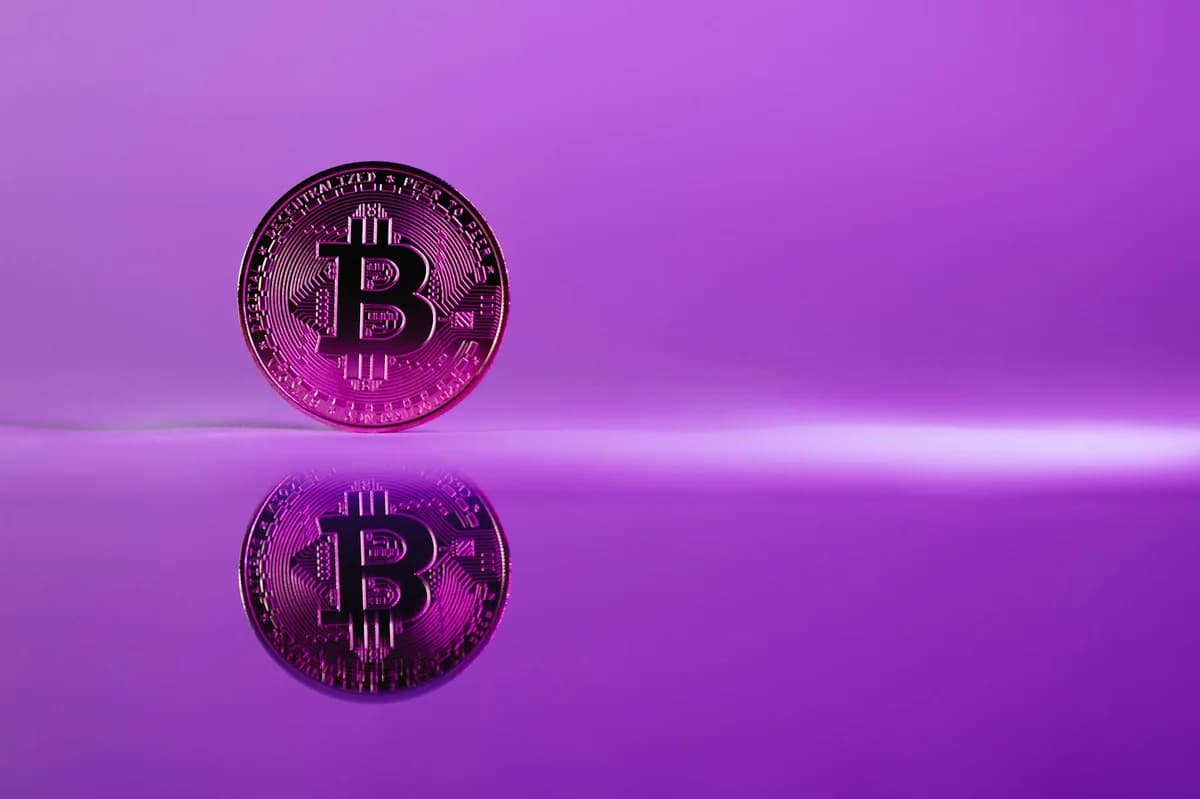 A striking image of a Bitcoin coin reflecting on a glossy surface against a vibrant purple background.