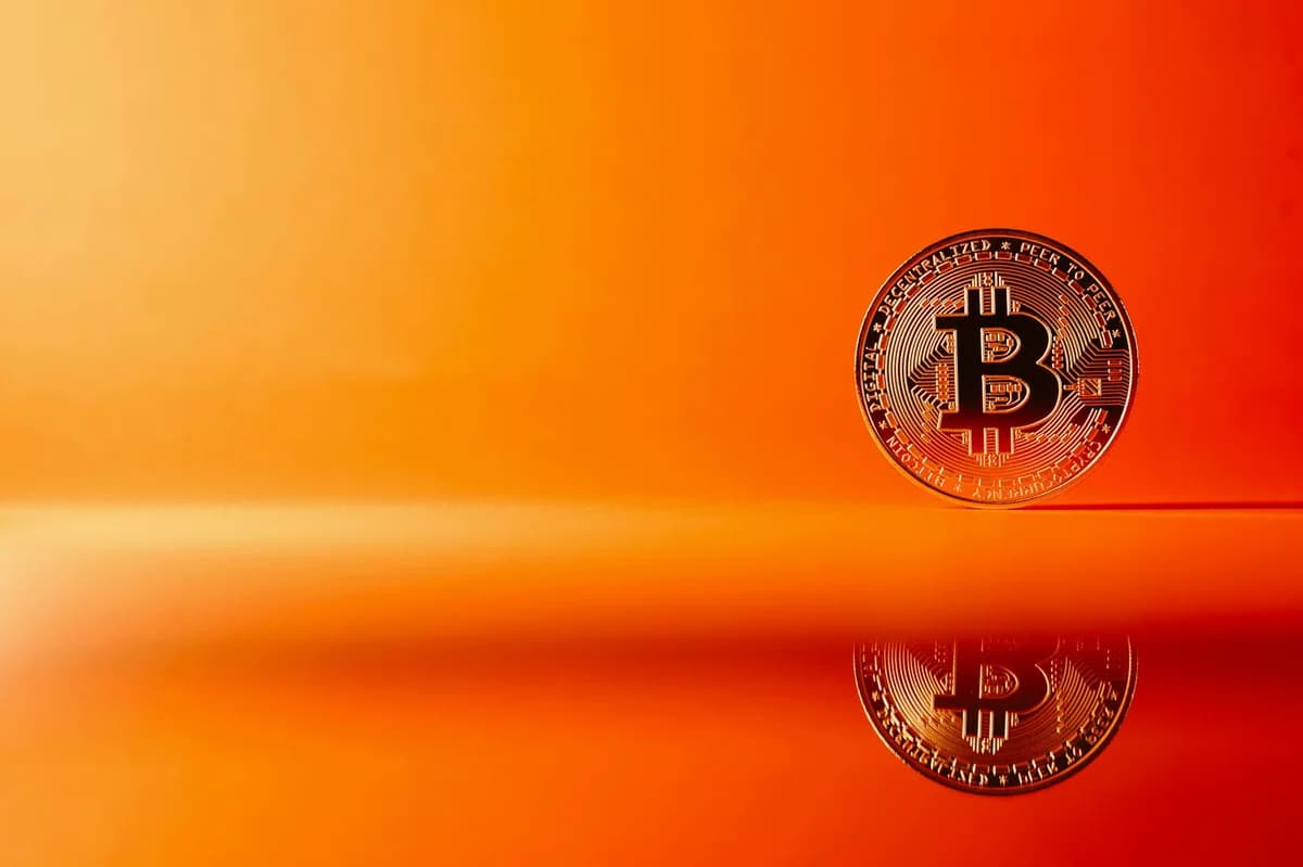 Golden Bitcoin with reflection on a bright orange background, representing digital currency concepts.