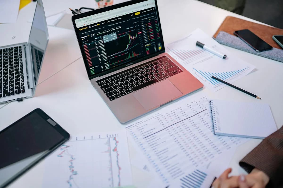 A professional tracks stock market trends using two laptops and a smartphone, showcasing digital finance tools.