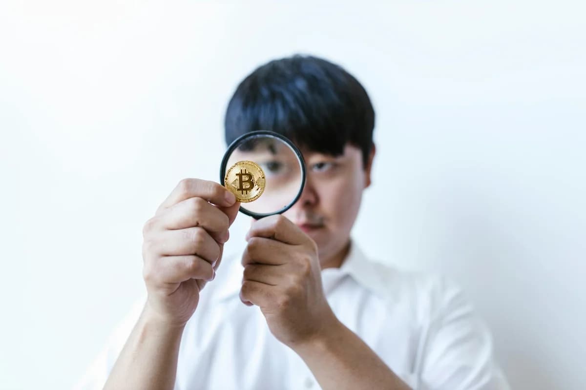 Close-up of a man examining a Bitcoin coin with a magnifying glass, symbolizing cryptocurrency analysis.