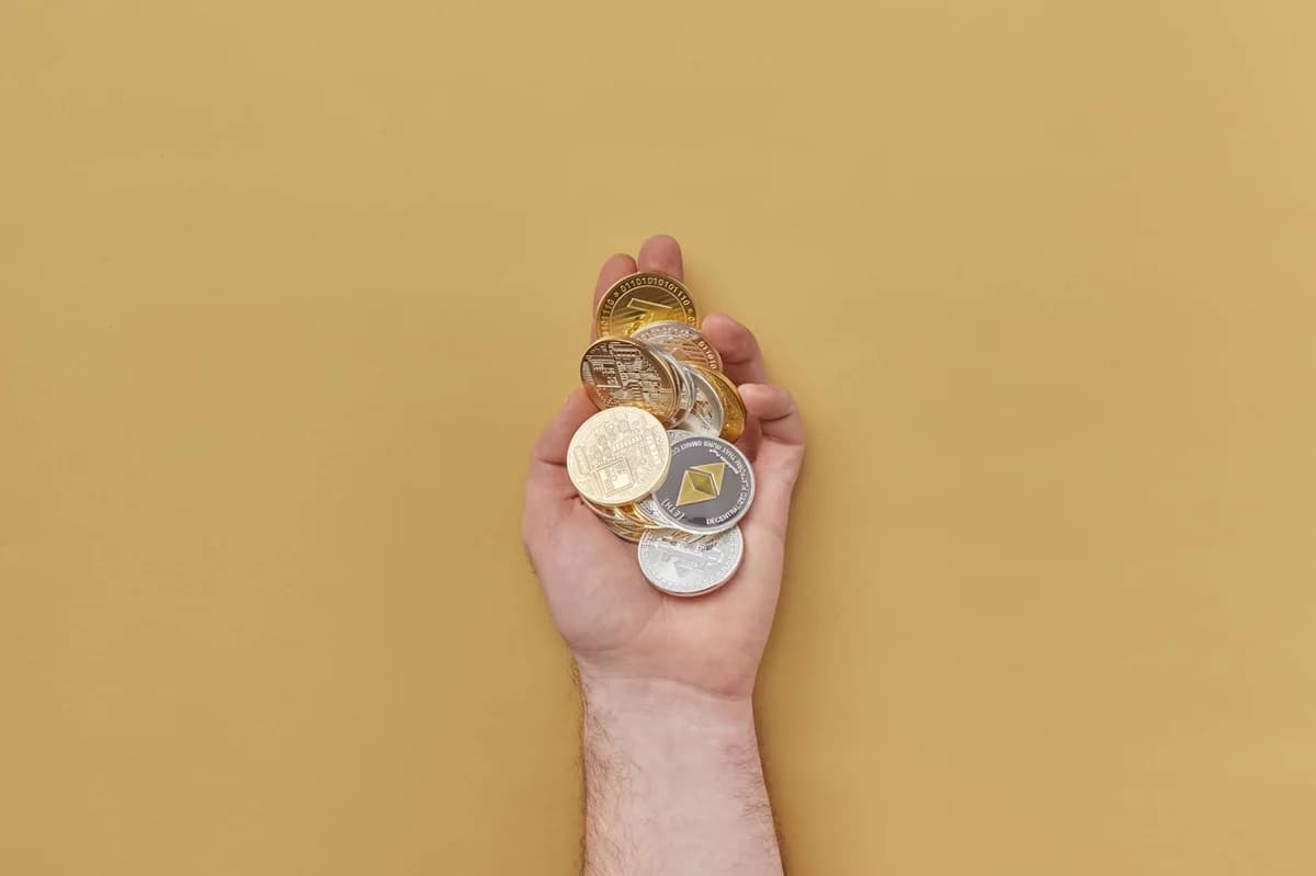 Close-up of a hand holding various cryptocurrency coins against a yellow background.